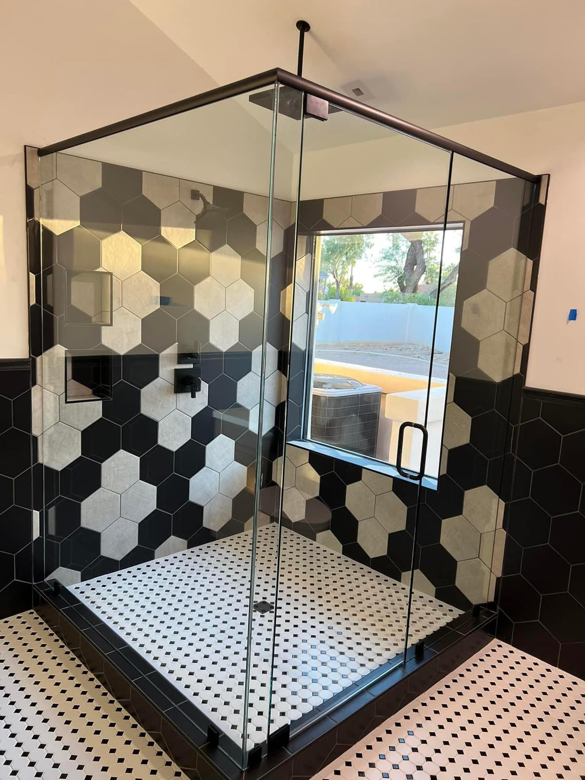 Corner glass shower with black, gray and white hex wall tile and black-framed enclosure