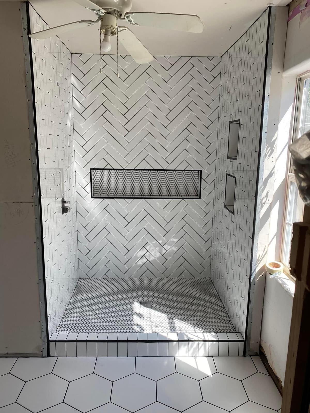 White herringbone shower under construction with black-trimmed niches and a small hex mosaic floor