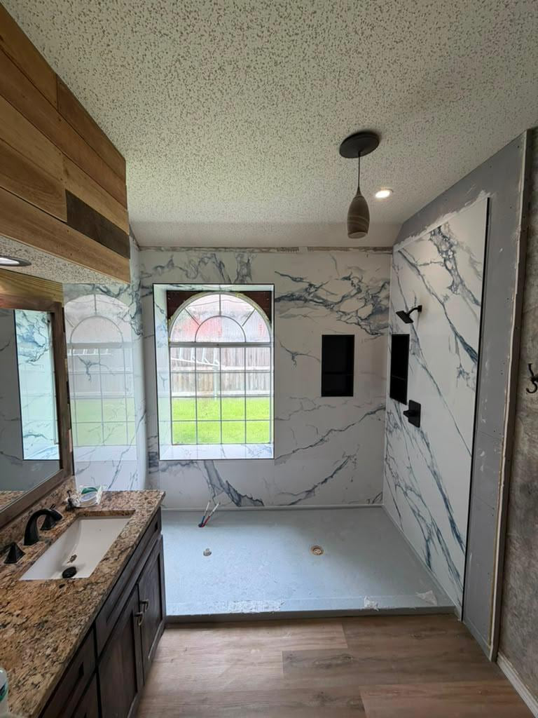 Open shower area under construction with white veined large-format wall panels, black niches and a gray shower base