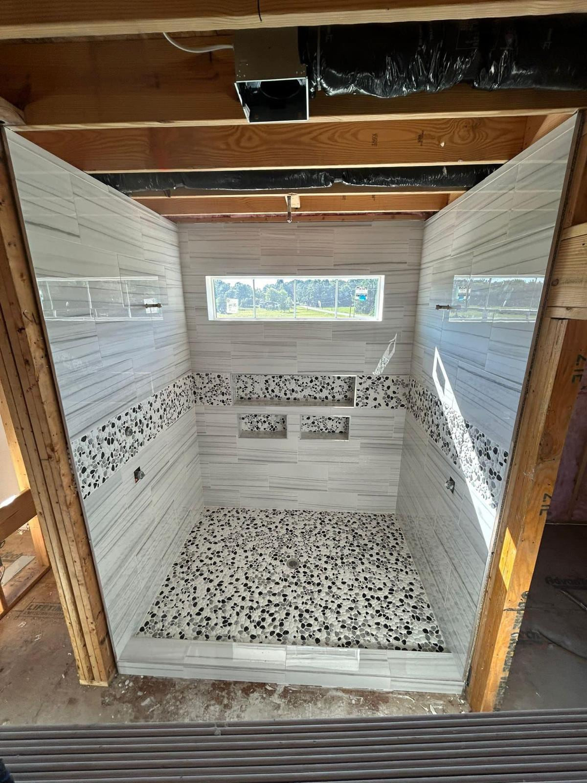 Shower under construction with light striped wall tile, pebble accent band, multiple niches and pebble floor