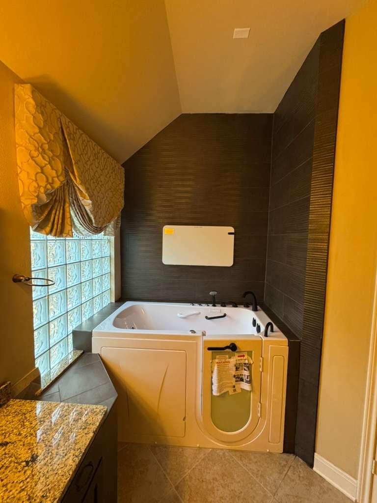 Walk-in tub installed against dark textured wall tile beside a glass-block window
