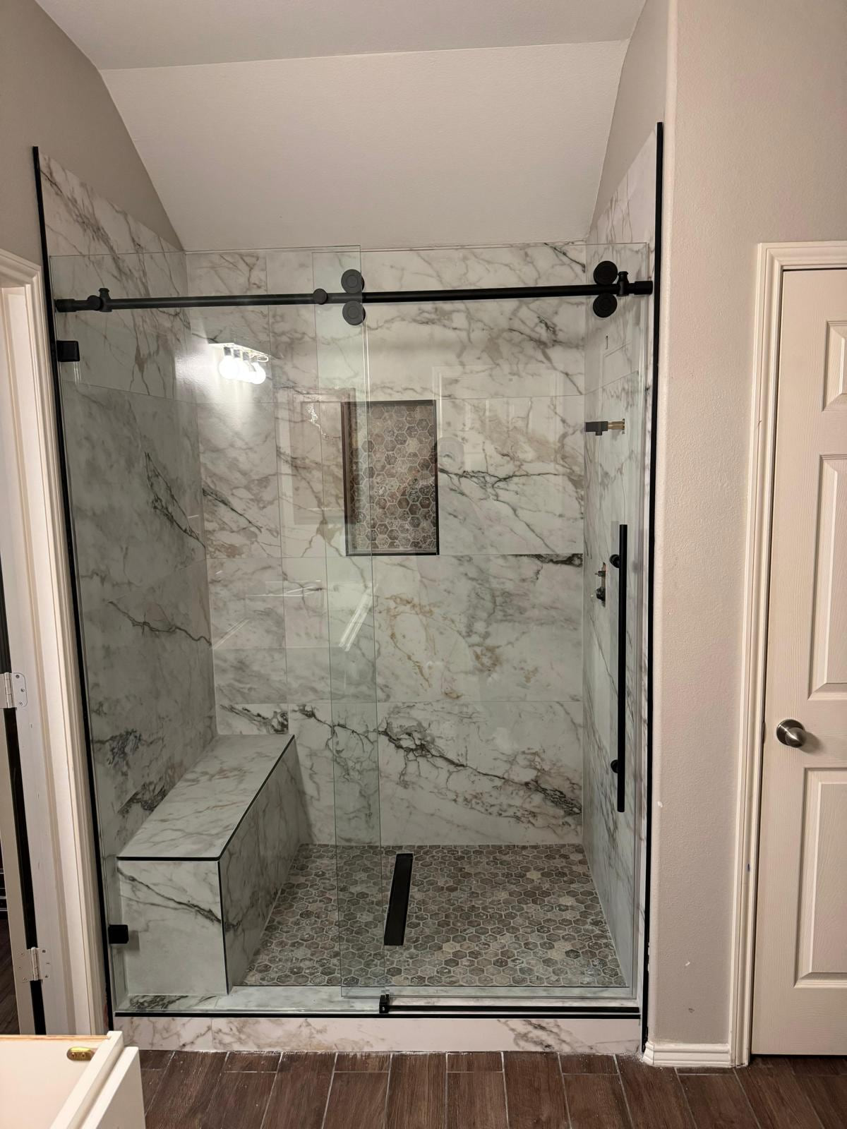 Walk-in shower with white veined surfaces, black-framed glass, built-in bench, niche and linear drain